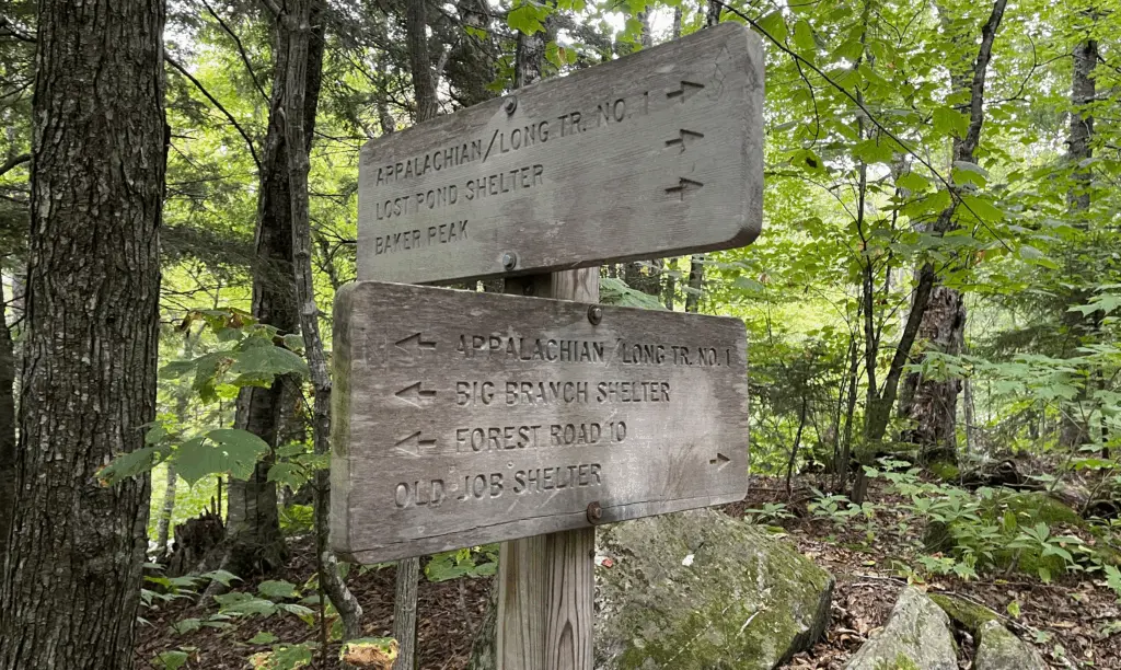 Sign post with two large weather worn boards on the Appalachian Trail with words and arrows pointing in different directions for destinations or direction. 